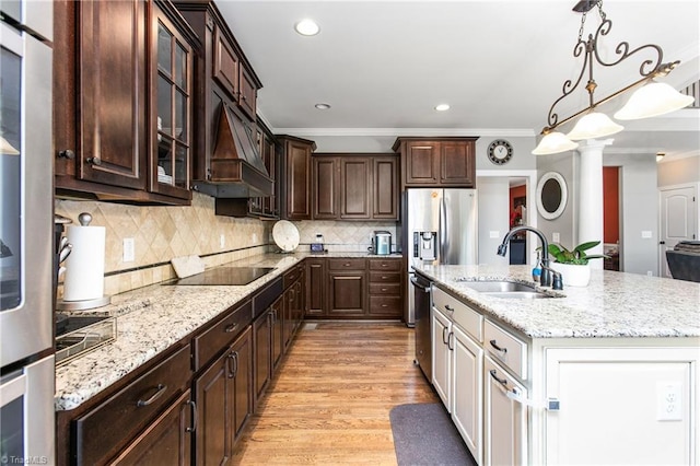 kitchen featuring sink, backsplash, light wood-type flooring, a center island with sink, and crown molding