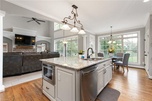 kitchen featuring decorative light fixtures, stainless steel dishwasher, sink, an island with sink, and white cabinets