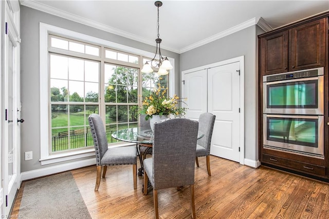 dining space with hardwood / wood-style flooring, crown molding, and an inviting chandelier