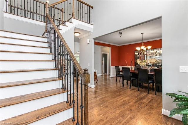 stairs featuring hardwood / wood-style flooring, ornamental molding, and a notable chandelier