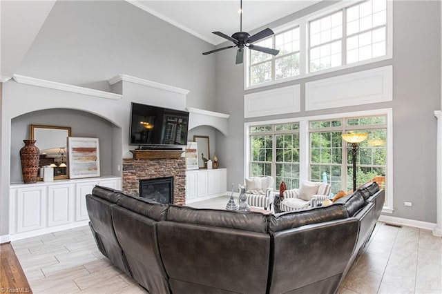 living room featuring ceiling fan, crown molding, a towering ceiling, and a stone fireplace