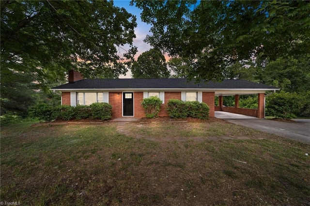 ranch-style home featuring brick siding, concrete driveway, a carport, a chimney, and a front yard
