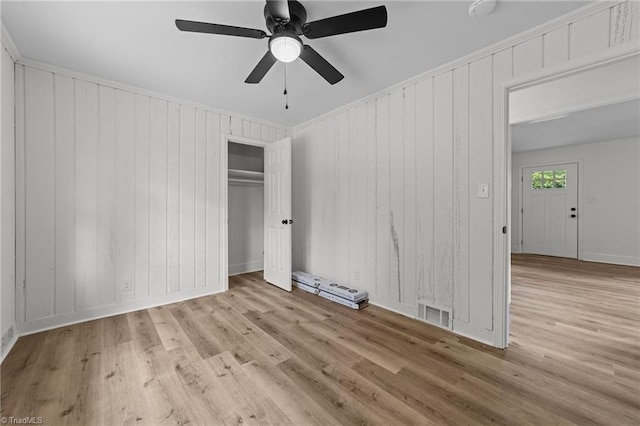 unfurnished bedroom with wood finished floors, a closet, a ceiling fan, baseboards, and wooden walls