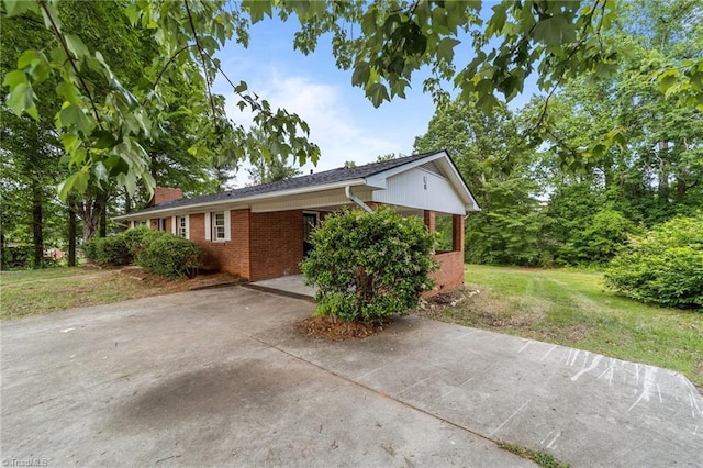view of side of home featuring brick siding, concrete driveway, a carport, a yard, and a chimney