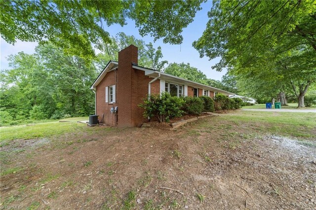 view of home's exterior with brick siding, a chimney, and central AC unit