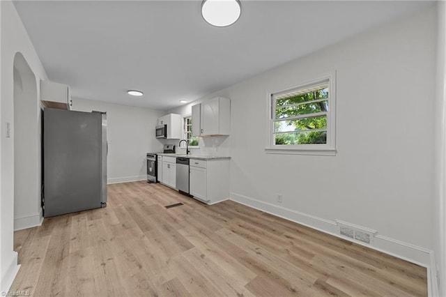 kitchen with stainless steel appliances, light countertops, a sink, white cabinetry, and baseboards