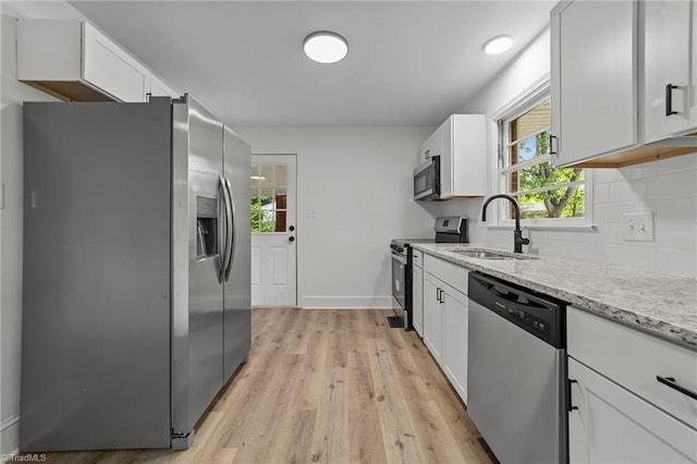 kitchen with appliances with stainless steel finishes, a sink, light wood-style floors, tasteful backsplash, and light stone counters