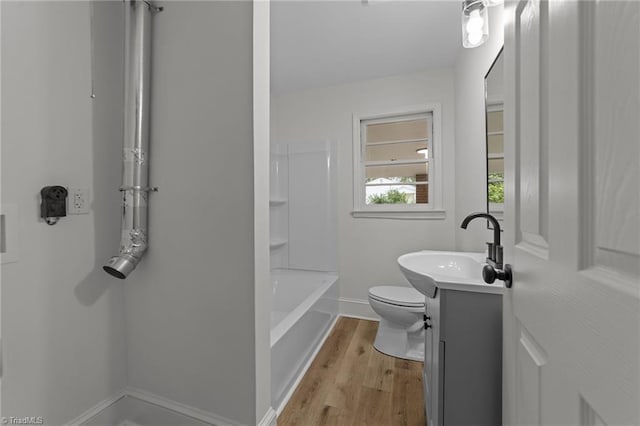 bathroom with vanity, toilet, baseboards, wood finished floors, and washtub / shower combination