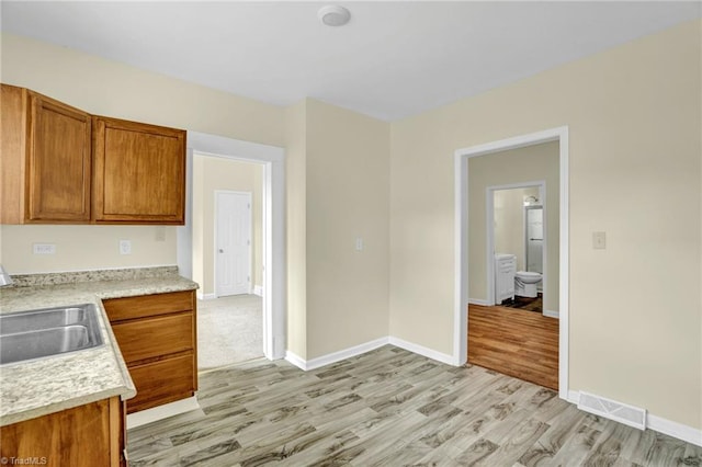 kitchen featuring visible vents, light countertops, light wood-style floors, brown cabinetry, and a sink