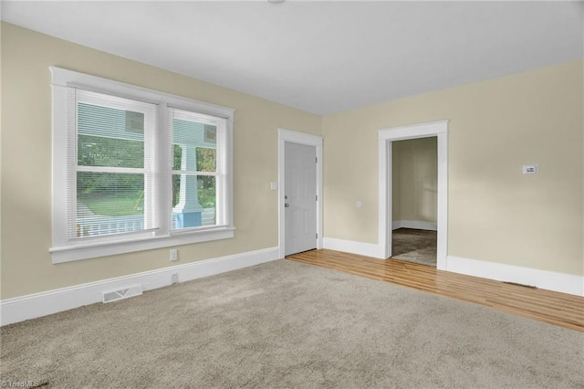 empty room featuring visible vents, wood finished floors, baseboards, and carpet floors