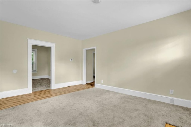 carpeted spare room featuring wood finished floors and baseboards