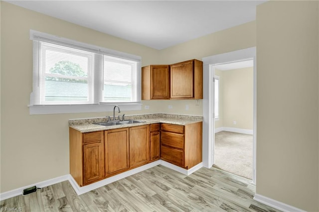 kitchen with baseboards, light wood-type flooring, light countertops, brown cabinetry, and a sink