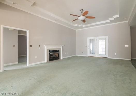 unfurnished living room with a tray ceiling, carpet, a fireplace, and baseboards