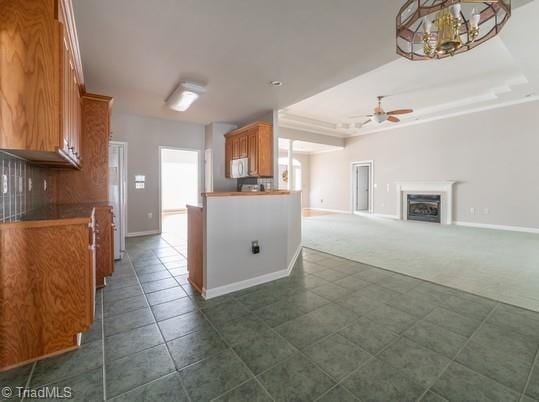 kitchen featuring brown cabinetry, white microwave, dark colored carpet, a fireplace, and ceiling fan with notable chandelier