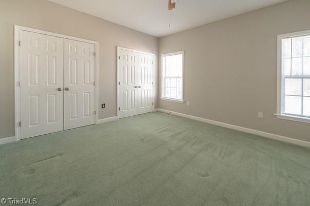 unfurnished bedroom with ceiling fan, carpet floors, two closets, and baseboards