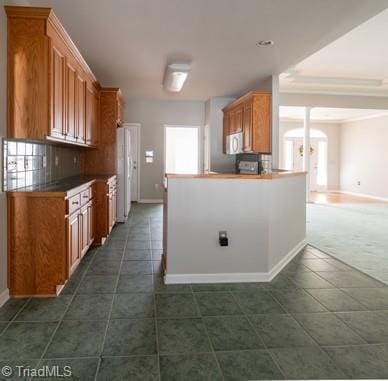 kitchen featuring white appliances, tasteful backsplash, baseboards, brown cabinetry, and dark tile patterned flooring