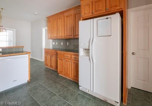 kitchen with brown cabinets, tile counters, backsplash, dark tile patterned flooring, and white appliances