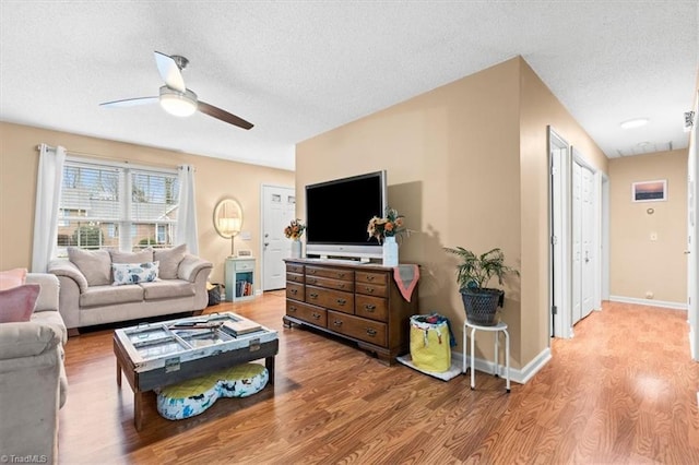 living room with ceiling fan, light wood-type flooring, and a textured ceiling