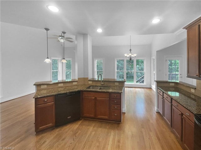 kitchen with a sink, black dishwasher, light wood-type flooring, dark stone countertops, and decorative light fixtures
