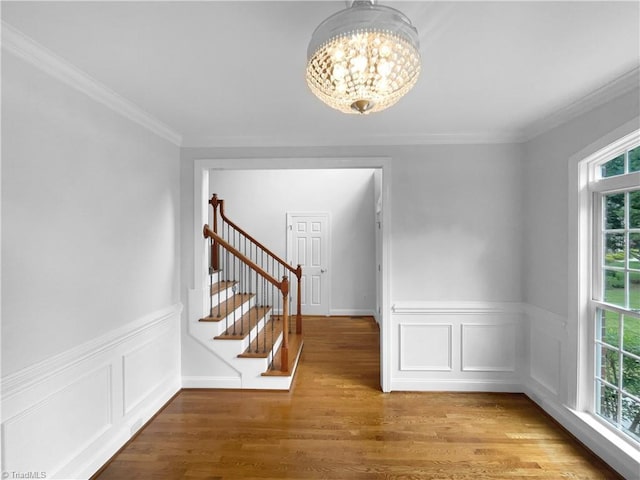 entryway with a chandelier, healthy amount of natural light, wood finished floors, ornamental molding, and stairs
