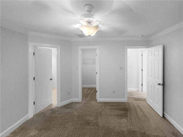 unfurnished bedroom with crown molding, a spacious closet, carpet floors, baseboards, and a closet