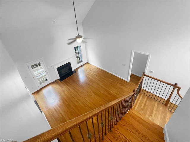 unfurnished living room with wood finished floors, a ceiling fan, high vaulted ceiling, a fireplace with flush hearth, and baseboards