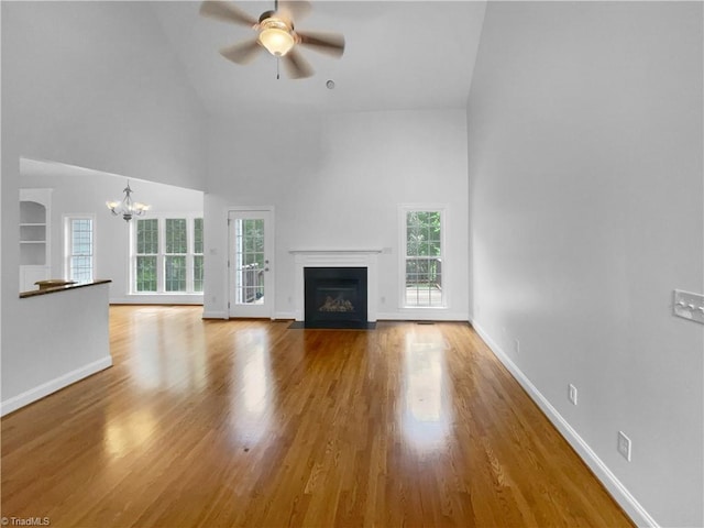 unfurnished living room featuring high vaulted ceiling, a ceiling fan, a fireplace with flush hearth, healthy amount of natural light, and a chandelier