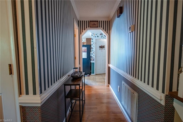 hallway with a textured ceiling, visible vents, wood finished floors, and ornamental molding