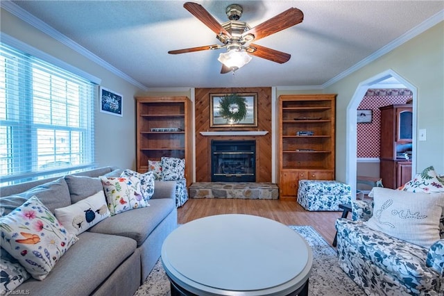 living area featuring a textured ceiling, ornamental molding, a fireplace, wood finished floors, and a ceiling fan