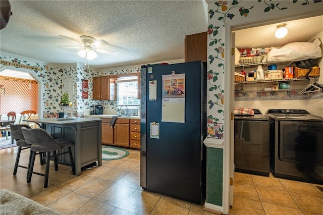 kitchen with brown cabinets, washer and clothes dryer, a breakfast bar area, a textured ceiling, and freestanding refrigerator
