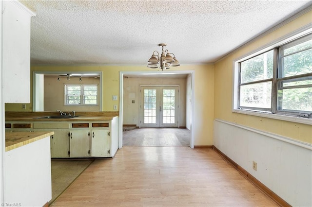 kitchen with plenty of natural light, decorative light fixtures, french doors, light wood-style floors, and a sink