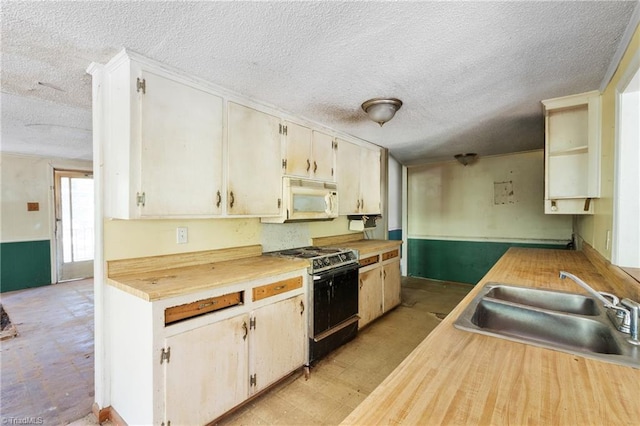 kitchen featuring a textured ceiling, white microwave, a sink, range, and light floors