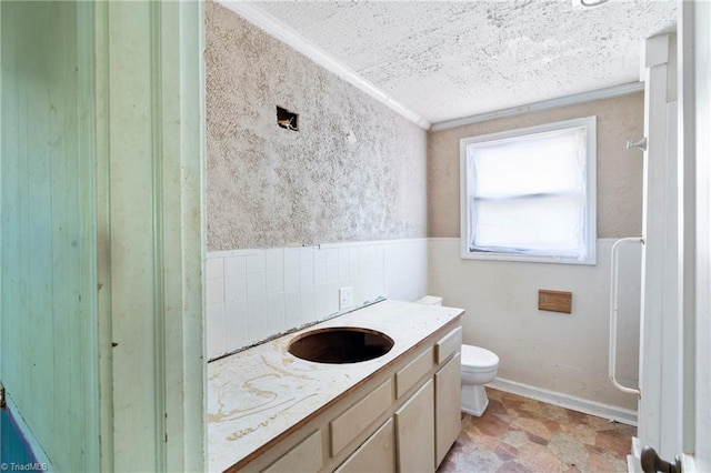 full bath featuring toilet, a wainscoted wall, a textured ceiling, vanity, and tile walls