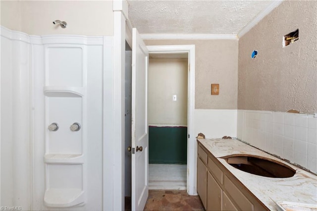 bathroom with ornamental molding, a textured wall, a textured ceiling, and vanity