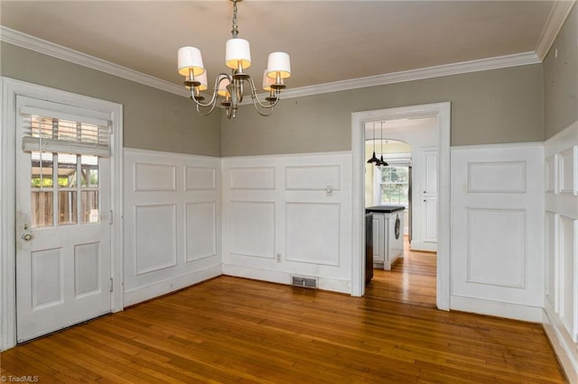 unfurnished dining area with wood-type flooring, an inviting chandelier, plenty of natural light, and ornamental molding