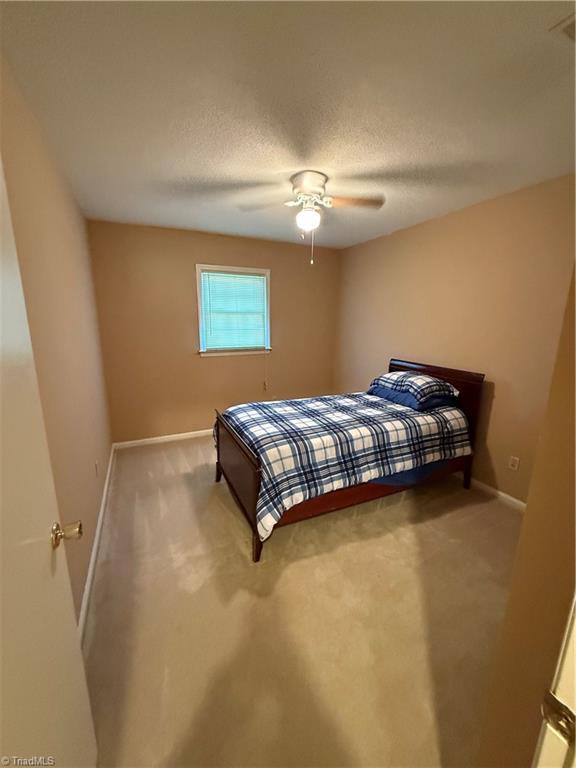 carpeted bedroom with ceiling fan and a textured ceiling