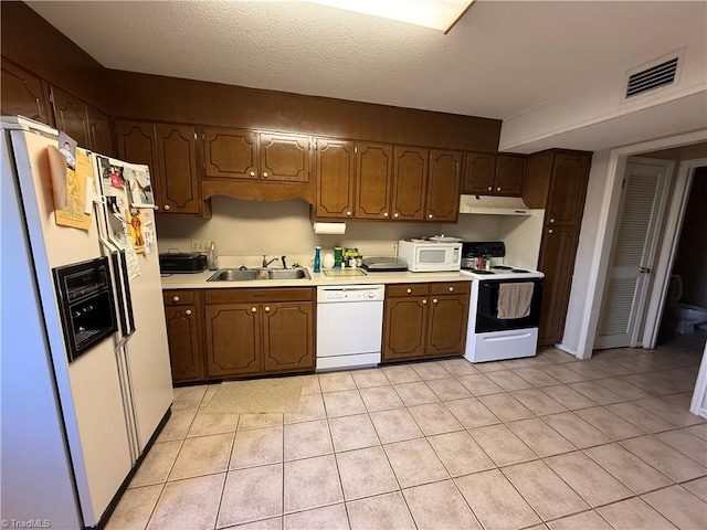 kitchen with light tile patterned flooring, a textured ceiling, white appliances, and sink