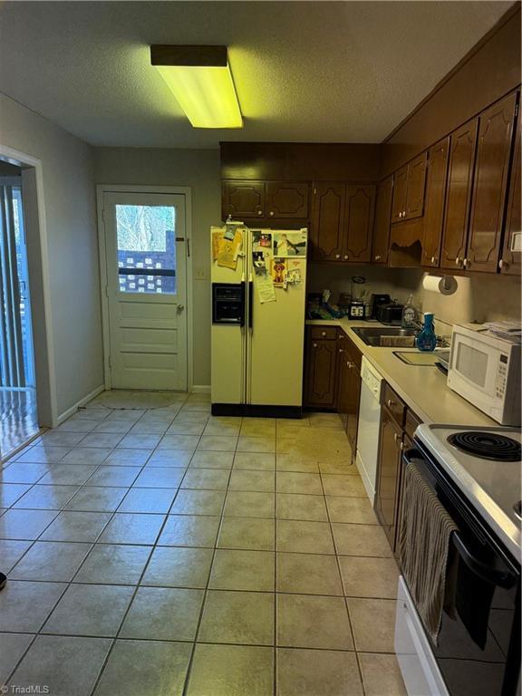 kitchen featuring light tile patterned flooring, a textured ceiling, white appliances, and sink