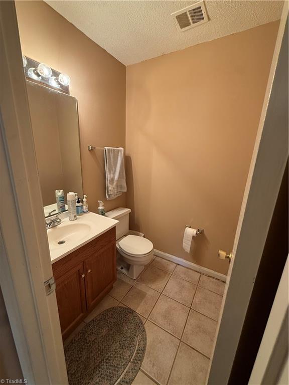 bathroom featuring tile patterned flooring, vanity, a textured ceiling, and toilet