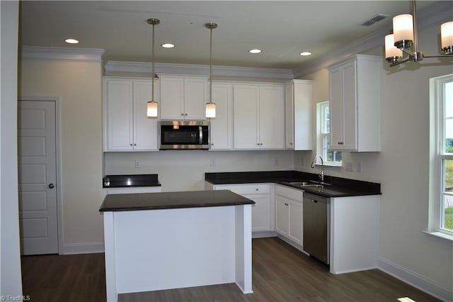 kitchen featuring crown molding, stainless steel appliances, dark countertops, visible vents, and a sink