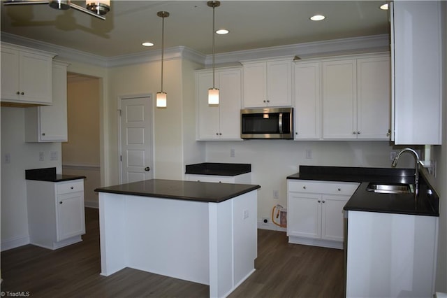 kitchen with a sink, ornamental molding, dark wood-style floors, stainless steel microwave, and dark countertops