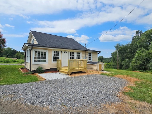 view of front of home featuring an outbuilding, roof with shingles, a wooden deck, a storage unit, and a front yard