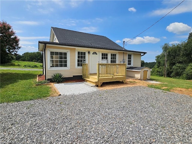 rear view of property with a deck, an outbuilding, roof with shingles, a lawn, and a storage unit