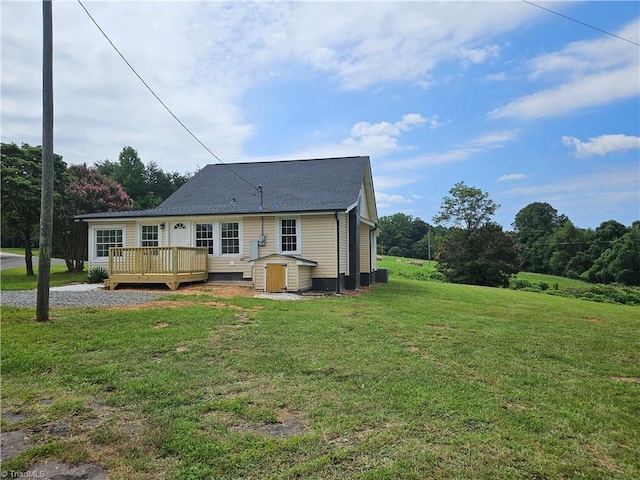 rear view of property featuring a shingled roof, a deck, and a yard