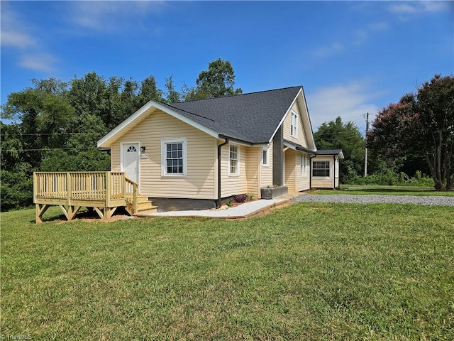 view of front of house featuring roof with shingles, a wooden deck, and a front lawn