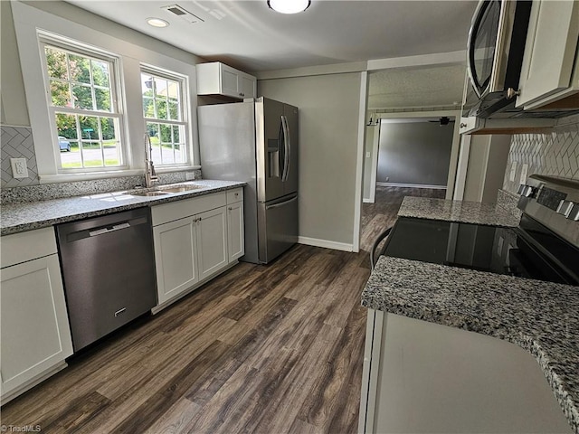 kitchen with stone countertops, dark wood finished floors, decorative backsplash, stainless steel appliances, and a sink