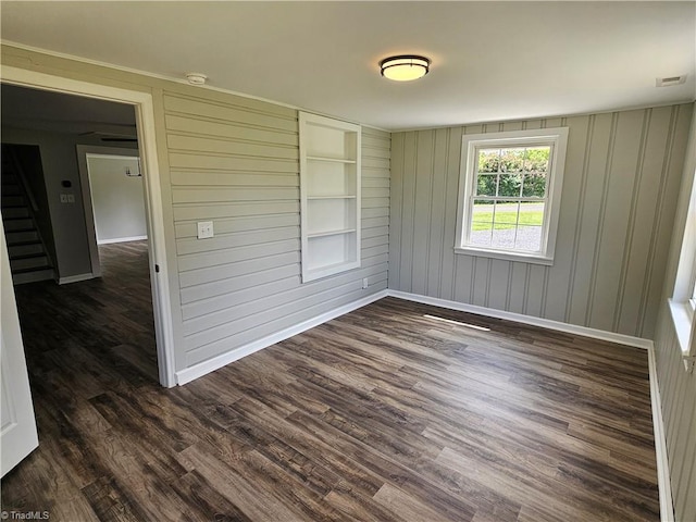 empty room with dark wood-style floors, stairs, visible vents, and baseboards