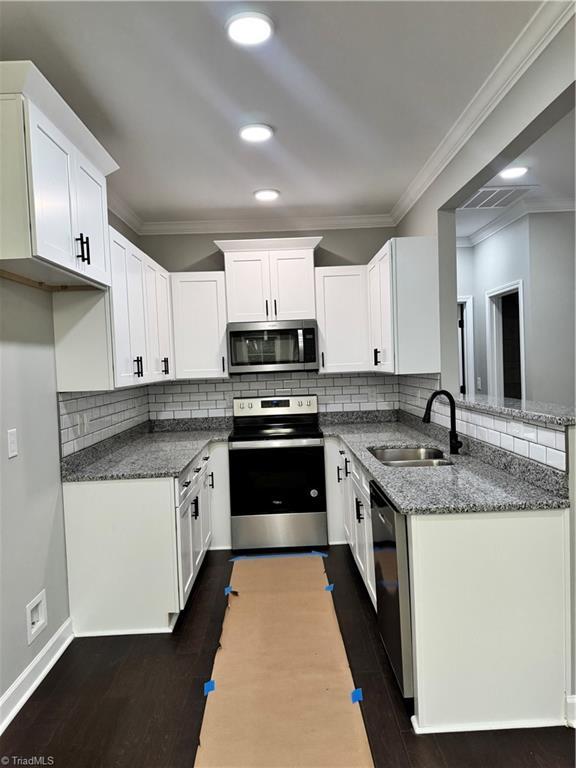 kitchen with appliances with stainless steel finishes, dark hardwood / wood-style floors, sink, and white cabinets