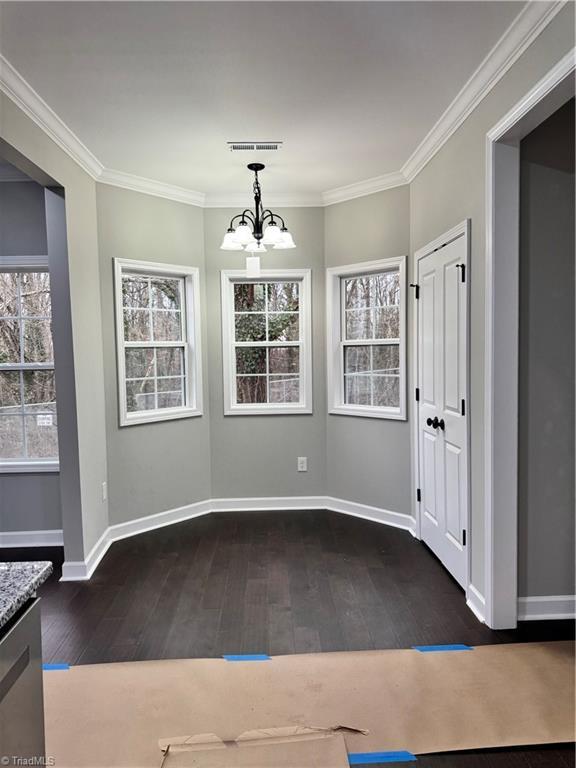 unfurnished dining area featuring crown molding, dark hardwood / wood-style flooring, and a notable chandelier