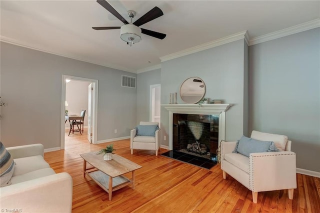 living room with ornamental molding, light wood-style floors, a tile fireplace, ceiling fan, and baseboards